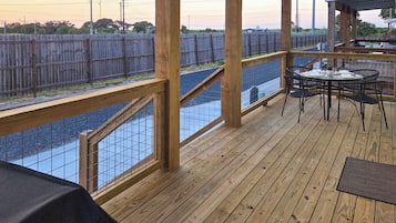 Una terraza de madera con una mesa y sillas, con vista a un área cercada con una masa de agua.