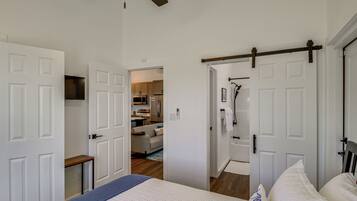 A bedroom with a bed, a ceiling fan, and a hallway leading to a kitchen.