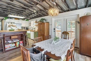Una cocina acogedora con armarios de madera, una mesa de comedor con mantel de encaje y una lámpara colgante.