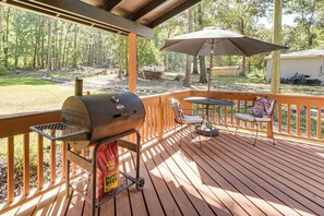 Una terraza techada al aire libre con una parrilla, una mesa con sillas y una sombrilla.