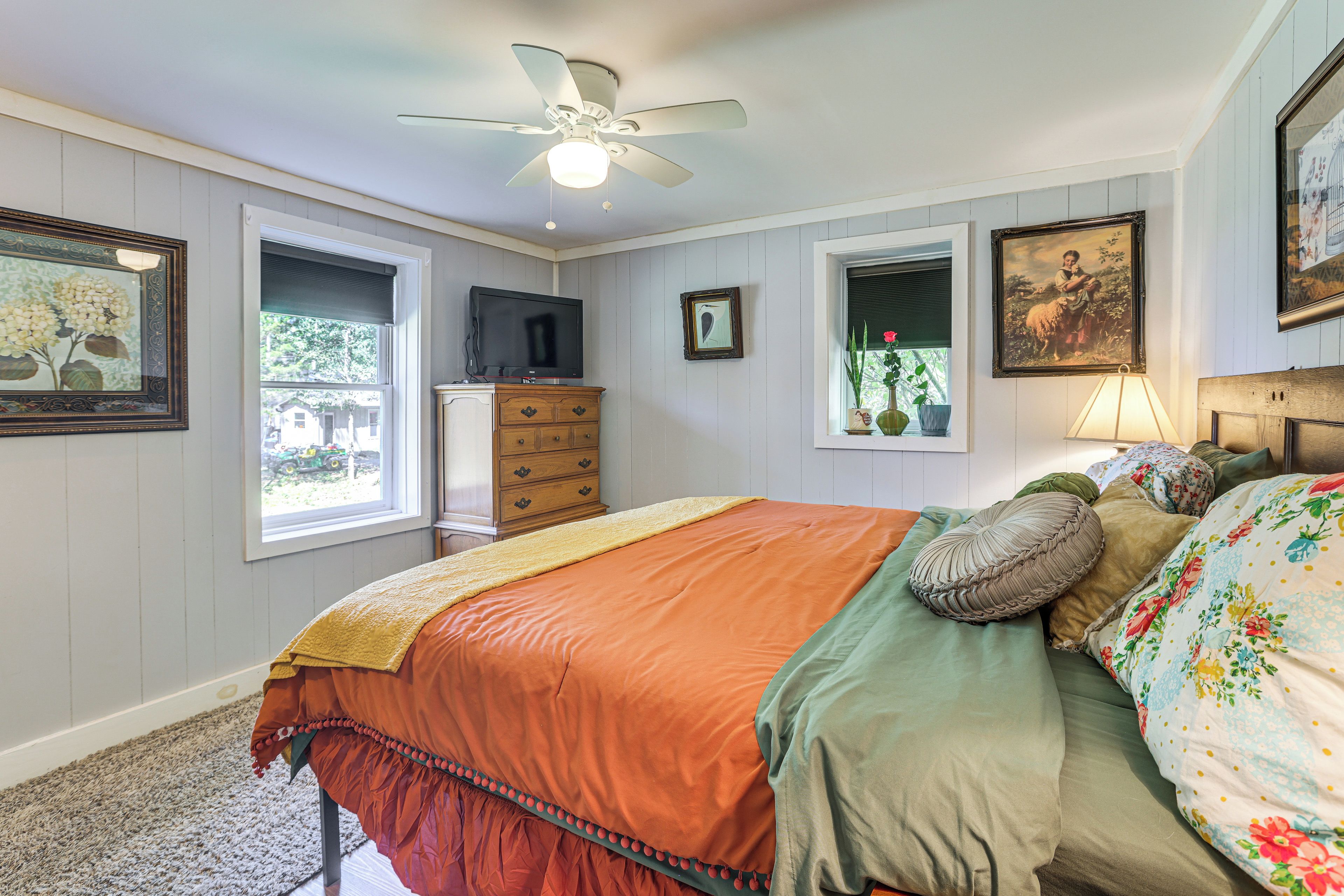 A bedroom with a bed, a dresser, a ceiling fan, a window, and wall-mounted artwork.