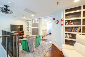 A modern living room with a flat-screen TV, a bookshelf, a green chair, a white sofa, and a staircase. - Walk to Waterfront! Old Town Alexandria Escape (Alexandria)