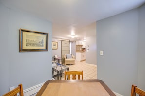 A dining area with a table and chairs, a framed picture on the wall, and a view into a kitchen area with cabinets and a tiled floor.