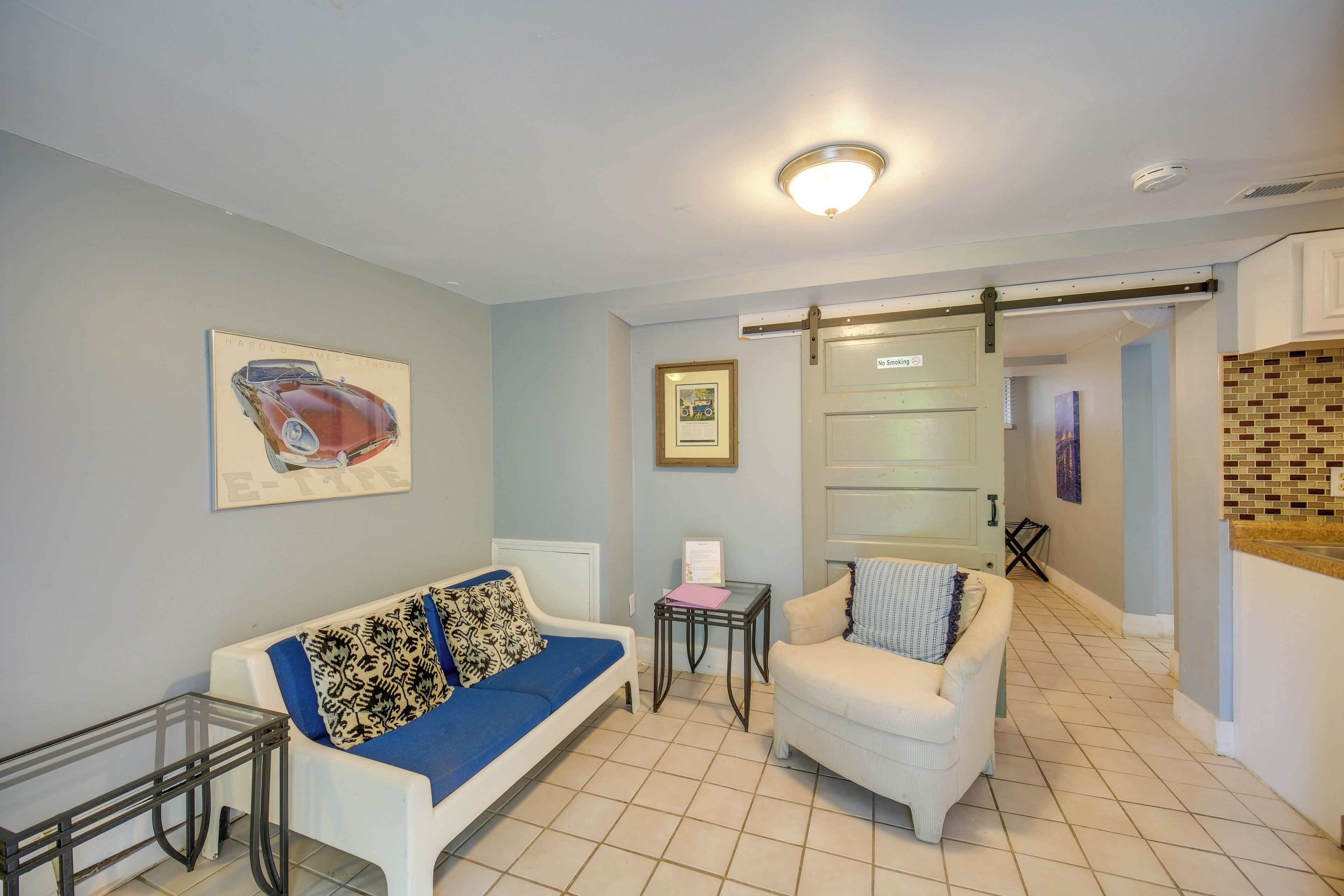 Un salon avec un canapé blanc, un coussin bleu, une petite table et un tableau encadré au mur.