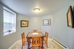 Un comedor con una mesa y sillas, una ventana con persianas y dos cuadros en la pared.