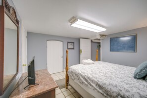 Quarto de hotel com cama, televisão sobre uma mesa de mármore, porta e ar condicionado fixado na parede.