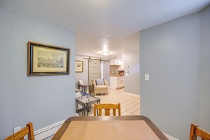 Un comedor con una mesa y sillas, un cuadro en la pared y vistas a una cocina con armarios y piso de baldosas.