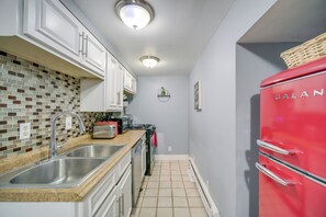 Una cocina con armarios blancos, un refrigerador rojo, salpicadero de azulejos y un lavamanos de acero inoxidable.