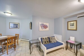 Una sala de estar con un sofá, una mesa de comedor con sillas y una mesita auxiliar con una lámpara.