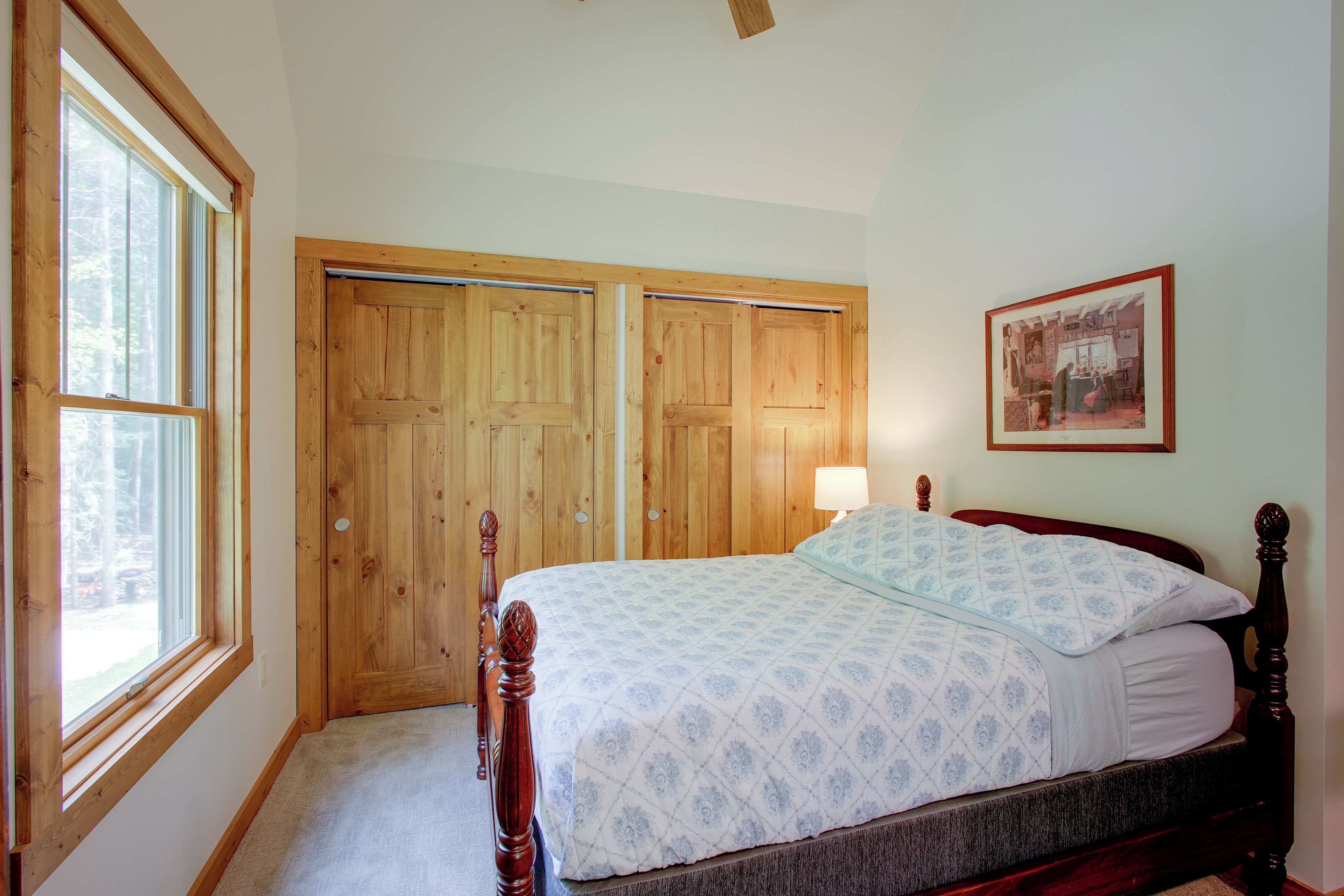 Quarto com cama de madeira, mesa de cabeceira, abajur e quadro na parede.