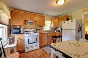A kitchen with wooden cabinets, a microwave, stove, refrigerator, and a dining table. - Private Beach Access! Lake Champlain Cabin (Plattsburgh)