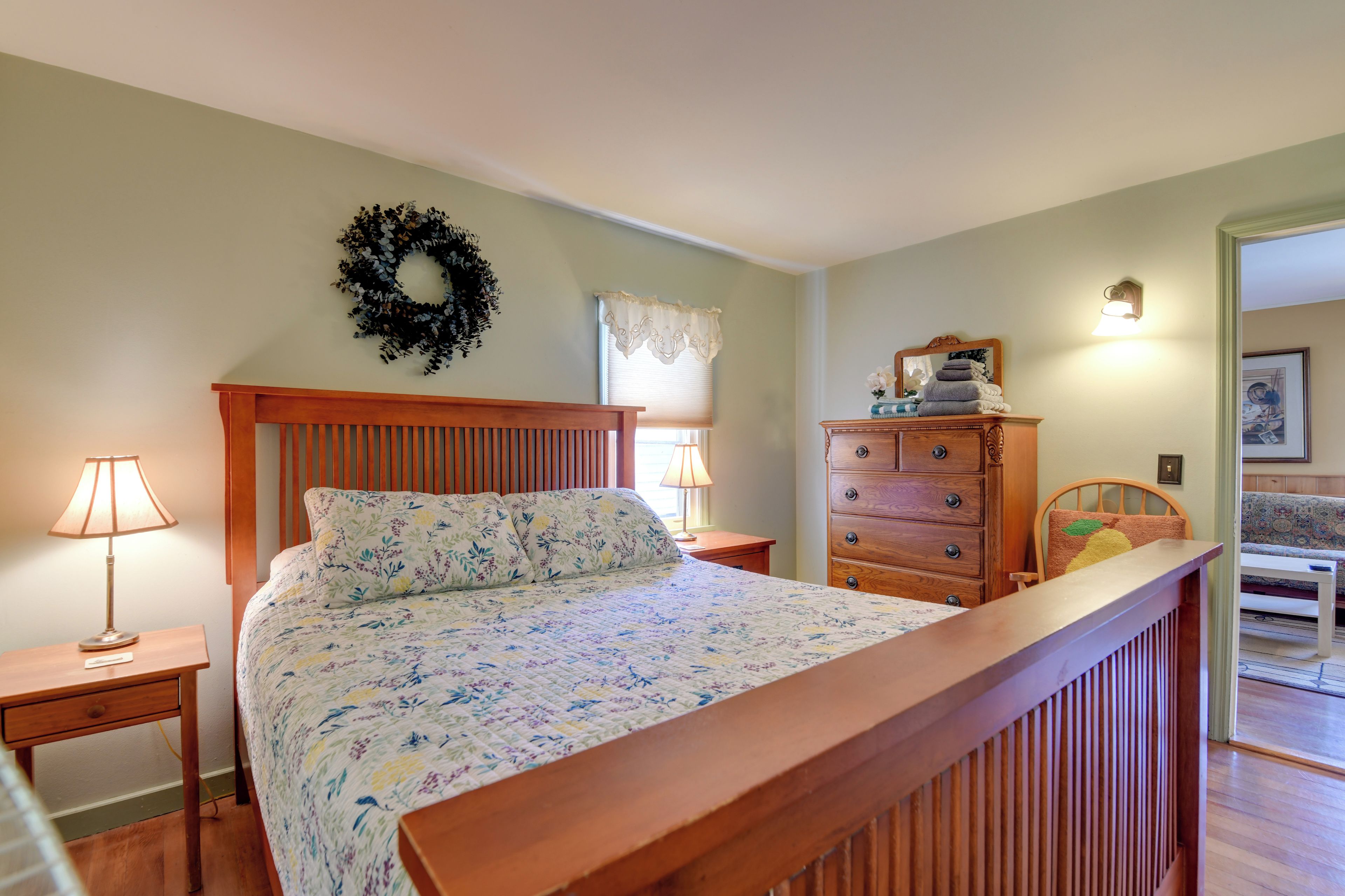 A bedroom with a bed, two nightstands, a dresser, a mirror, and a door leading to another room.