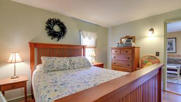 A bedroom with a bed, two nightstands, a dresser, a mirror, and a door leading to another room.