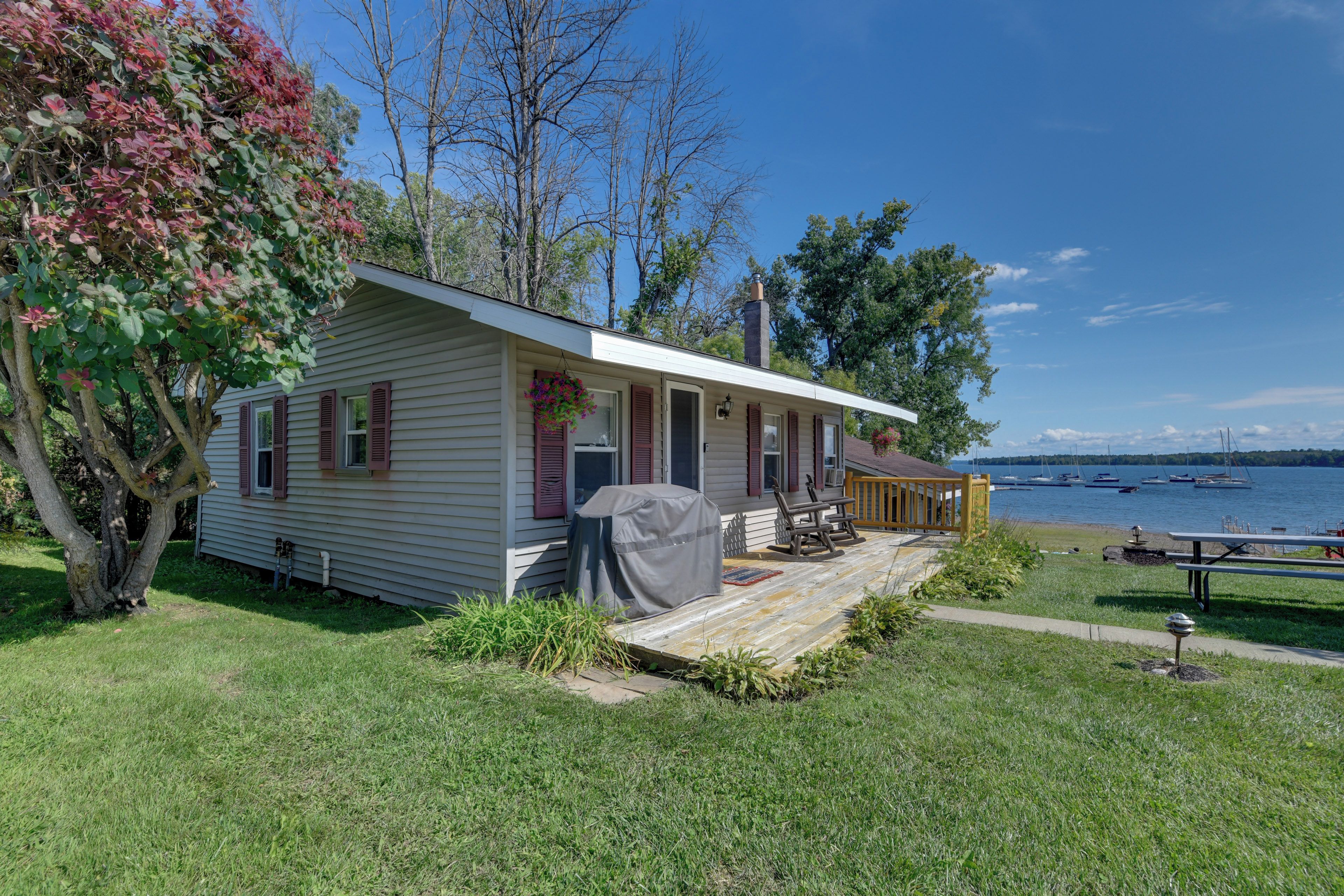 A single-story house with a covered porch, a grill, and a view of a lake with boats.