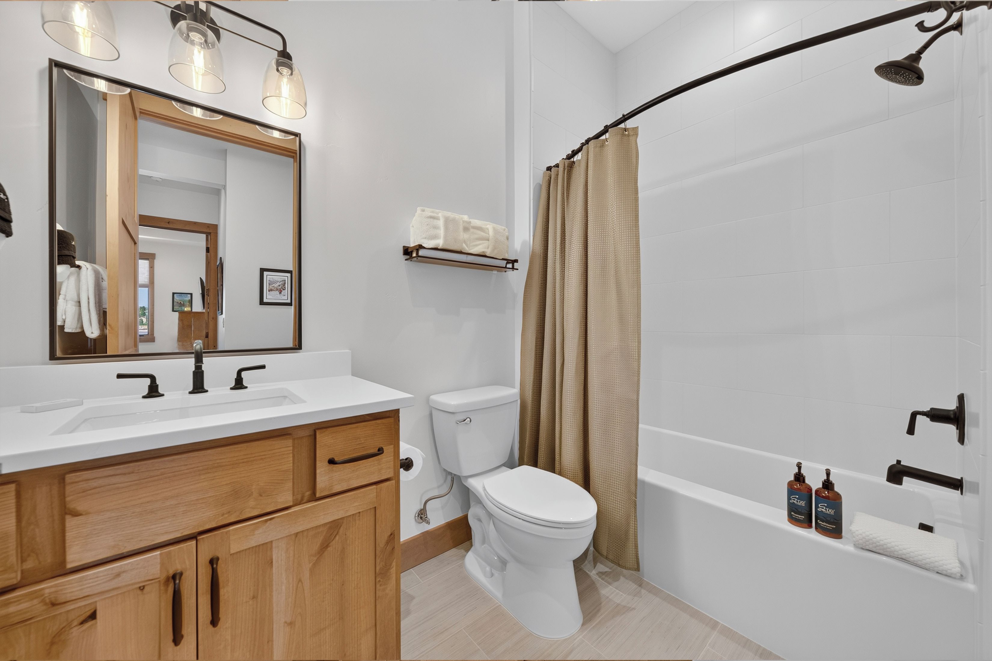A modern bathroom with a white sink, wooden vanity, a toilet, a bathtub, and a shower with a curved glass door.