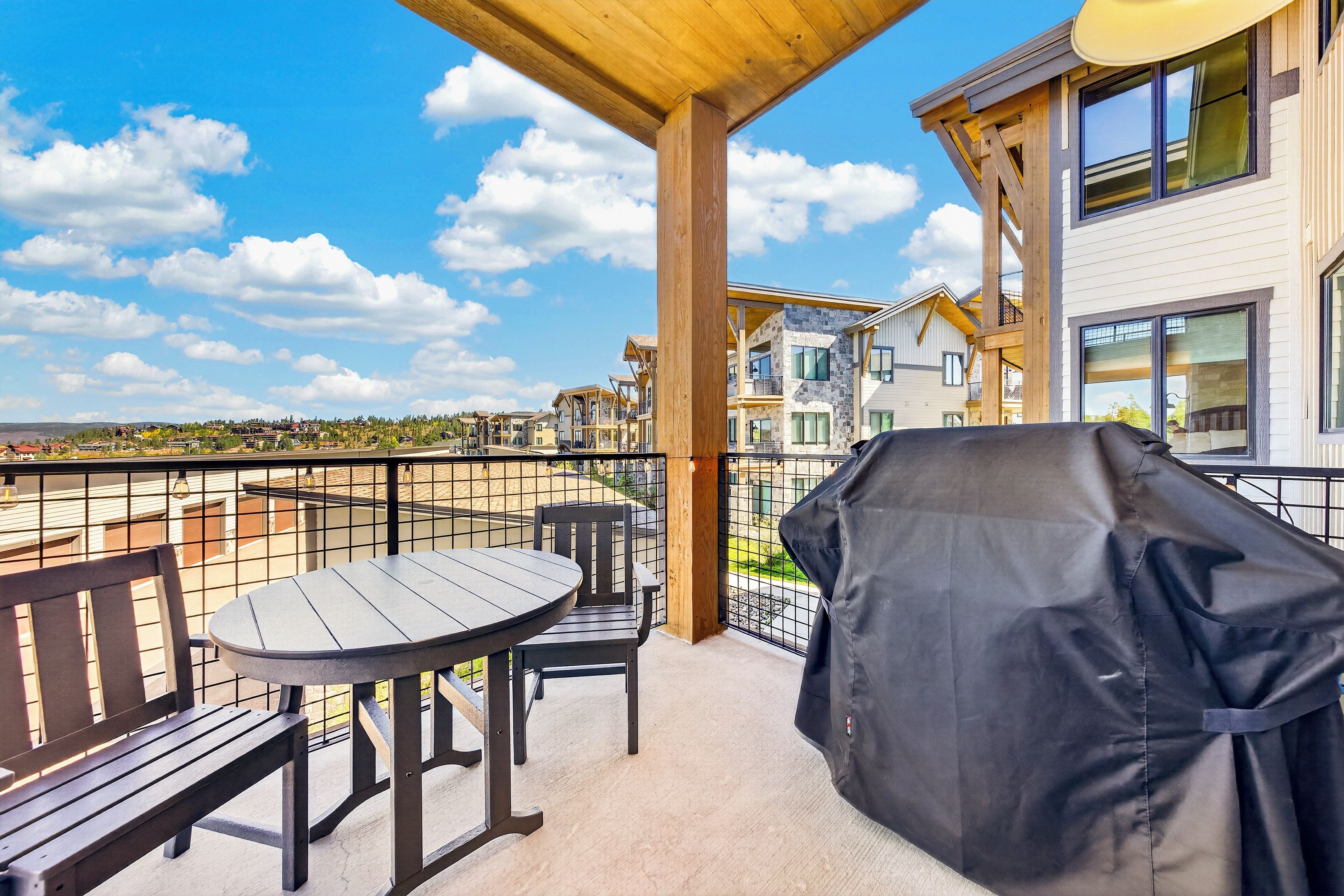 A balcony with a table and chairs, a grill, and a view of a residential area.
