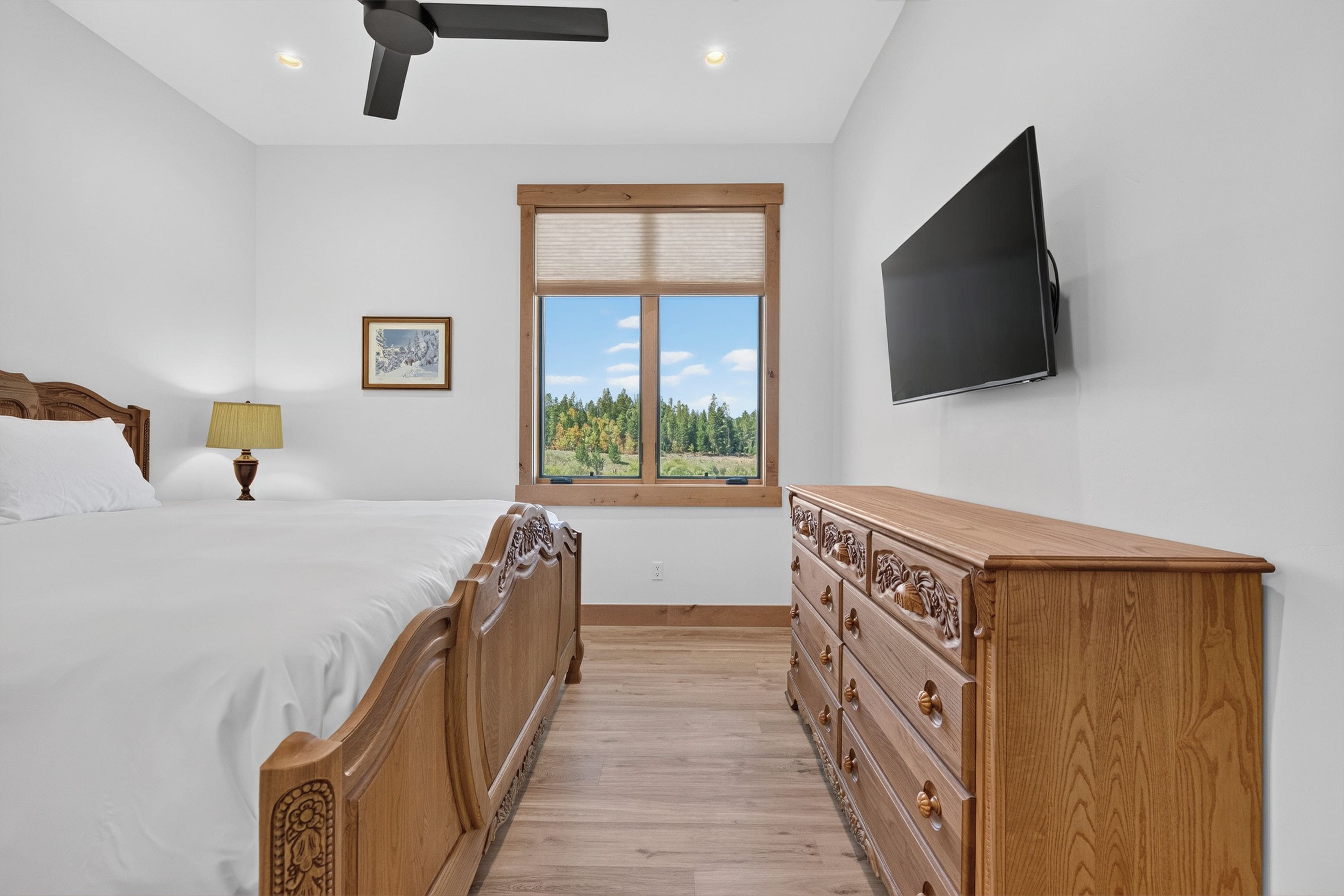 A bedroom with a bed, dresser, TV, window, and ceiling fan.