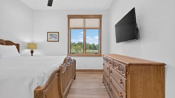 A bedroom with a bed, dresser, TV, window, and ceiling fan.