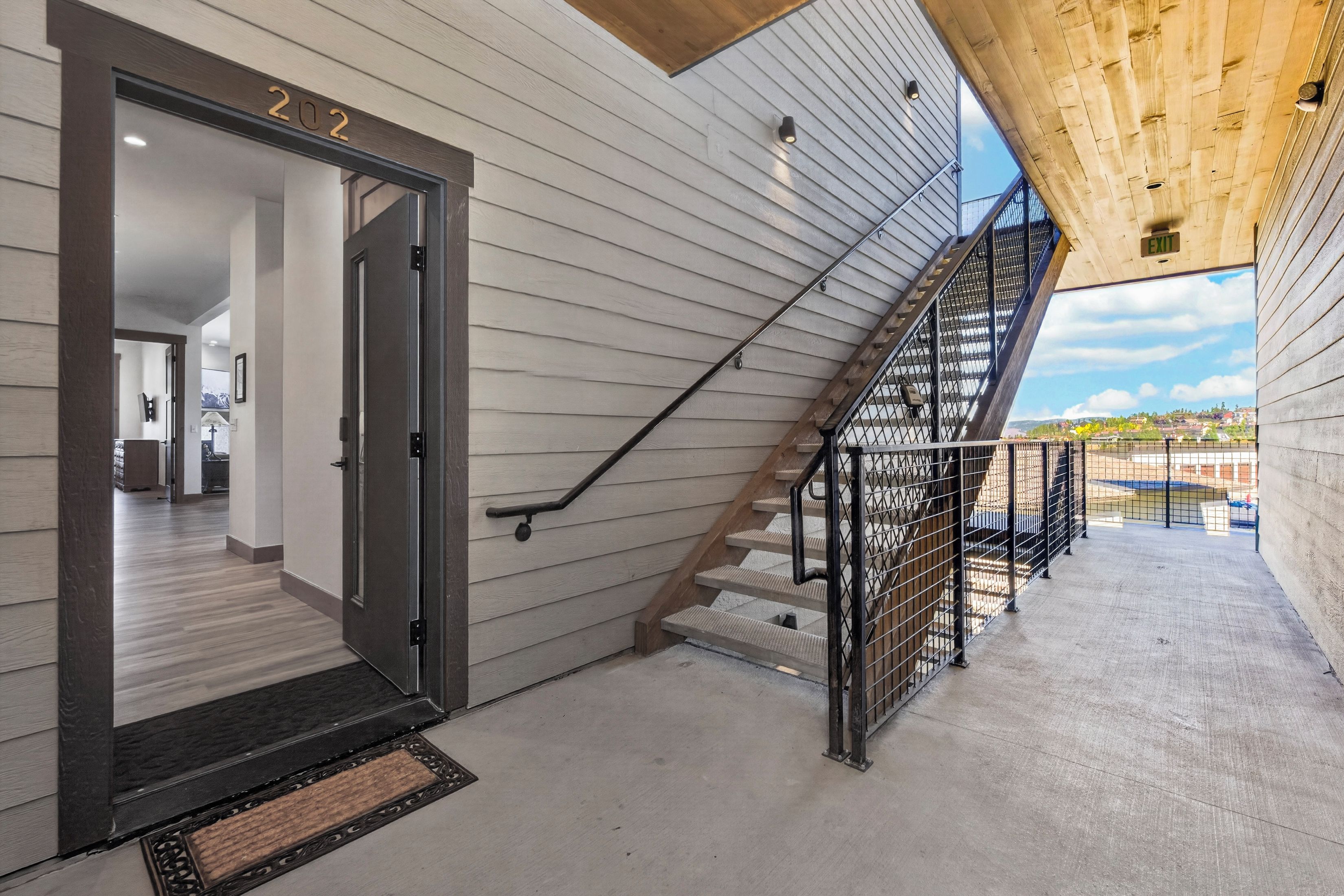 A modern interior with a staircase leading to a balcony, a door labeled '202', and a view of the outside.