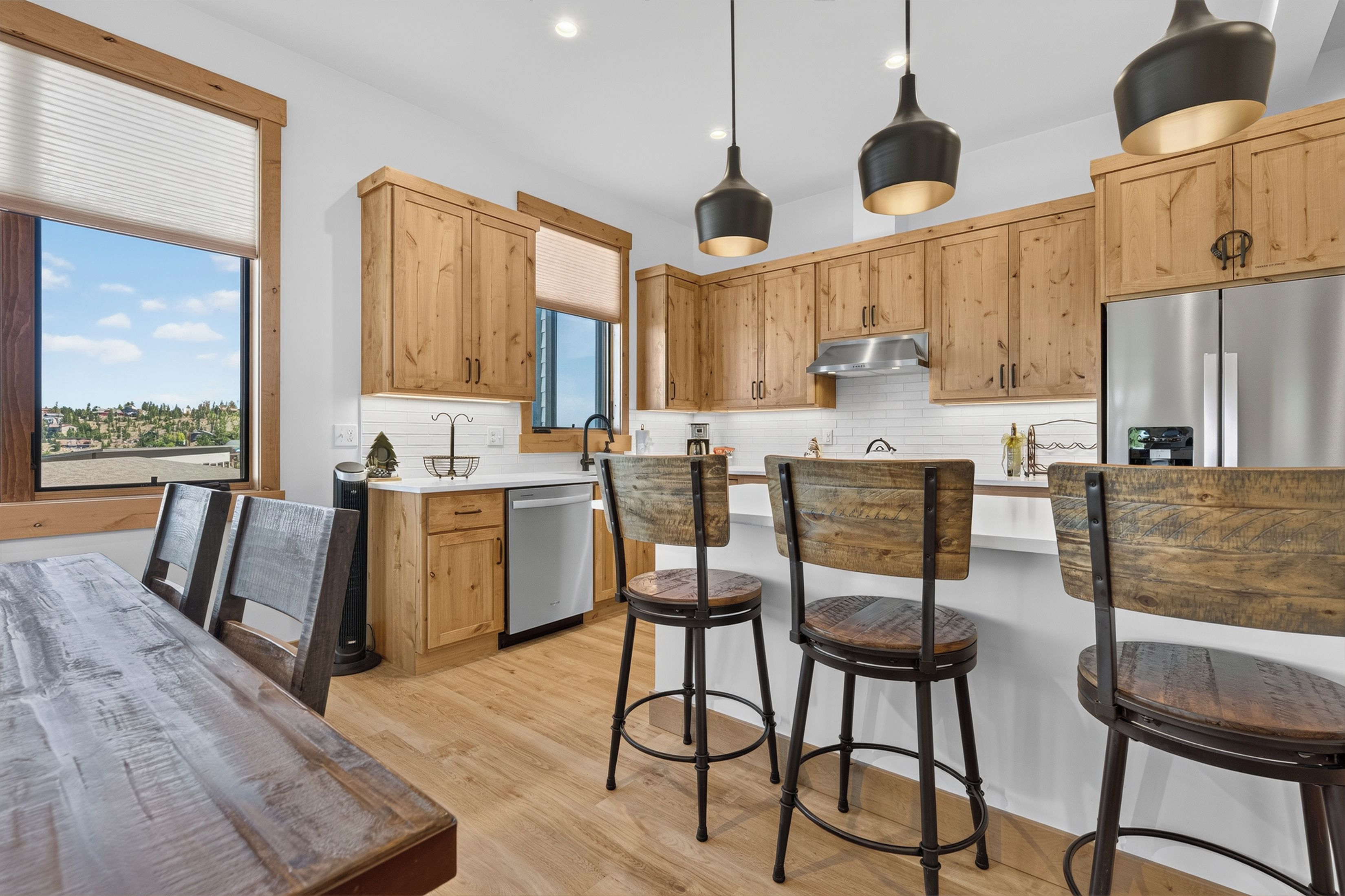 A modern kitchen with wooden cabinets, a stainless steel refrigerator, and a dining area with a wooden table and chairs.