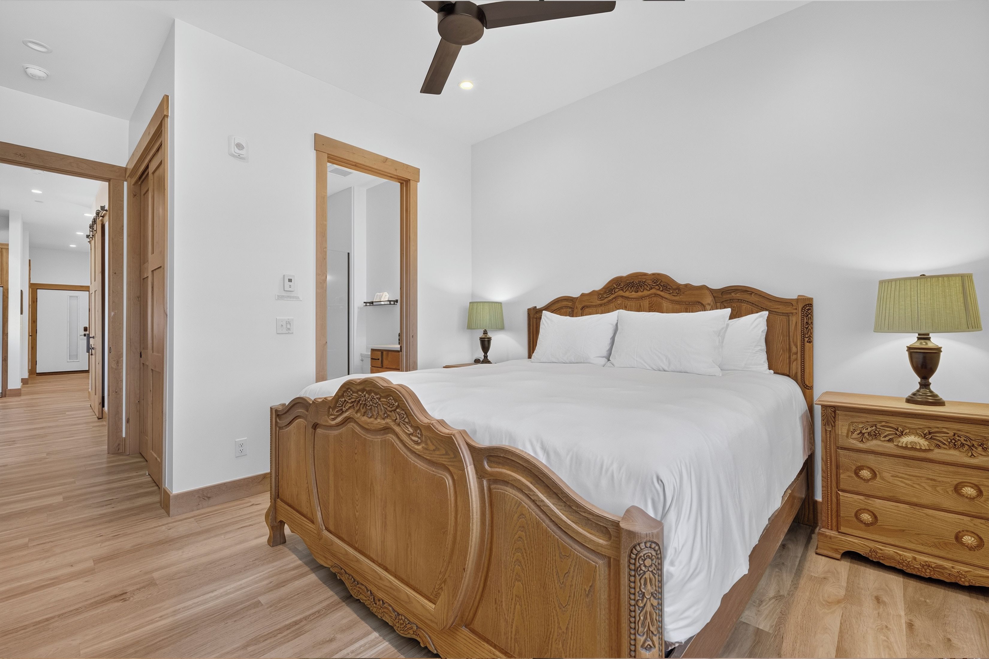 A bedroom with a wooden bed, bedside lamps, and a ceiling fan.
