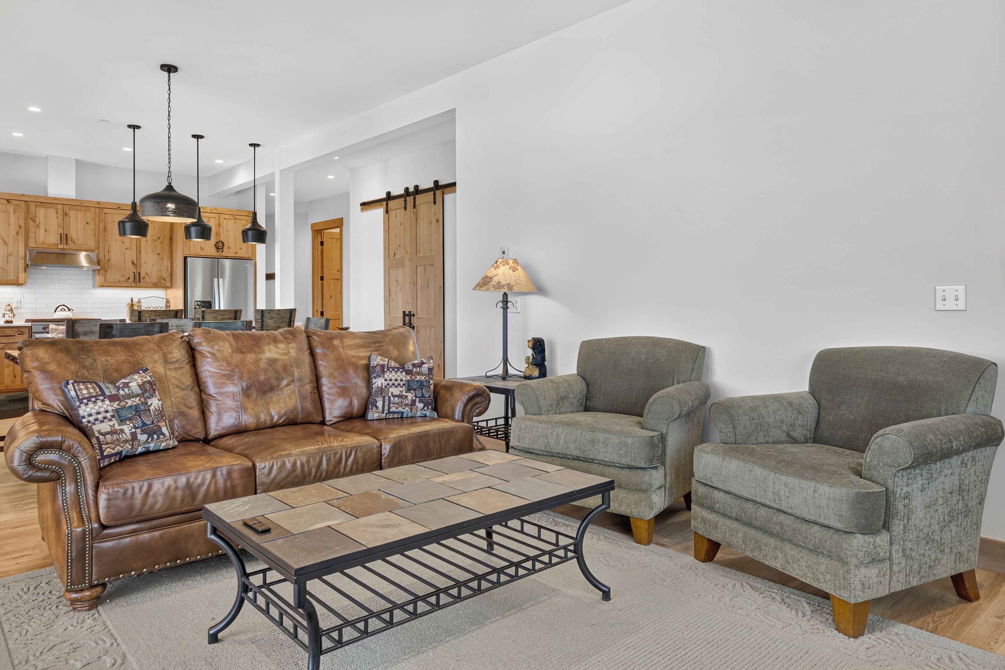A living room with a brown leather sofa, two grey armchairs, a coffee table, and a lamp.
