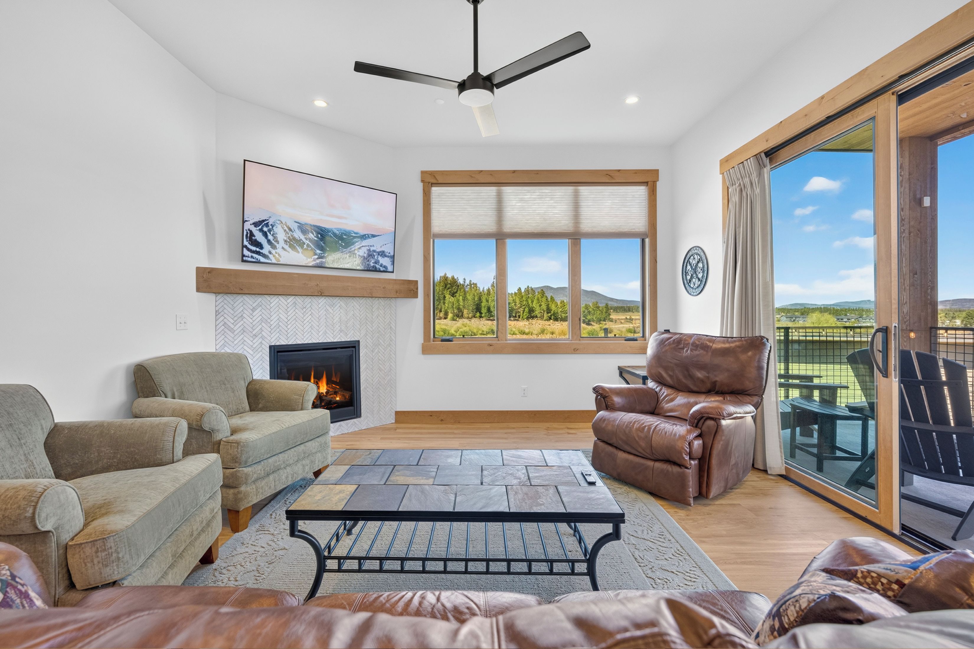 A spacious living room with a fireplace, comfortable seating, a large window with a scenic view, and a ceiling fan.