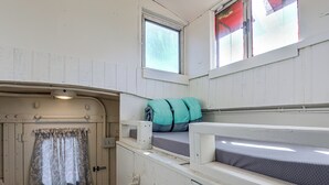 Una cabana petita i ben il·luminada amb una porta, un finestret i una llitera amb almoadines.