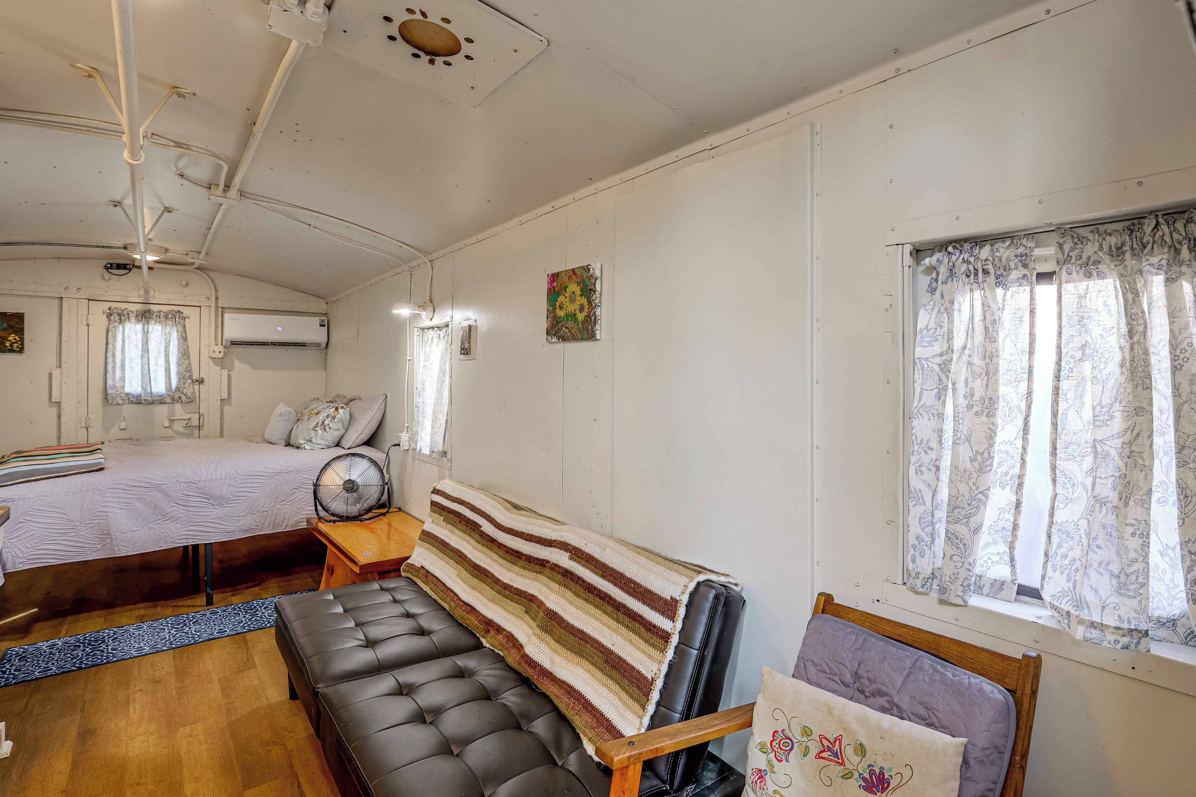 A room with a bed, a bench, a fan, and a window with curtains.