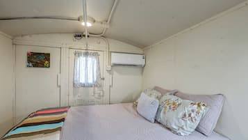 A room with a bed, a window with curtains, an air conditioning unit, and a wall-mounted artwork.