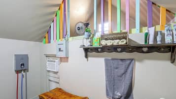 A room with a wooden bench, a towel hanging on the wall, a shelf with toiletries, and a fan.
