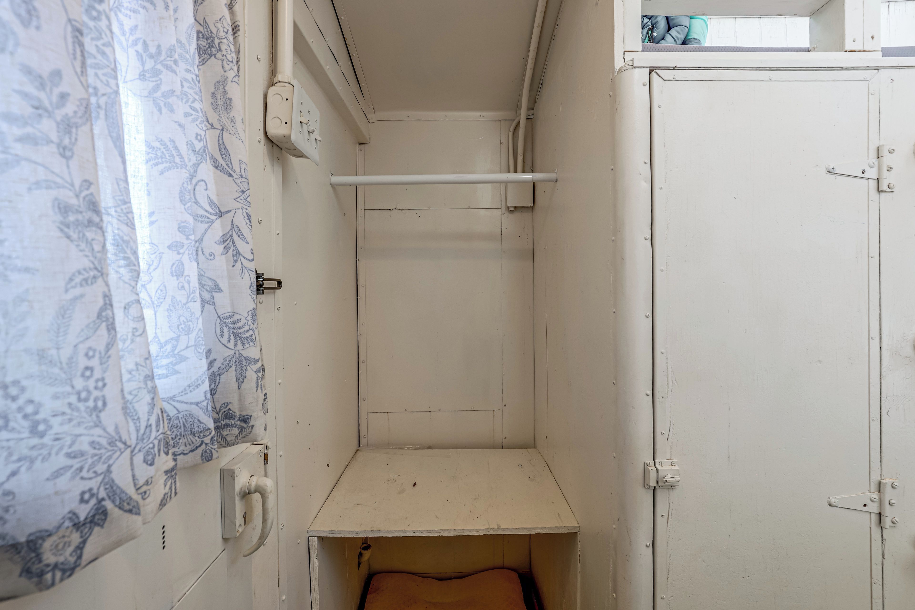 A narrow room with a single bed, a small shelf, and a door.