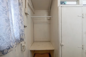 A narrow room with a single bed, a small shelf, and a door.