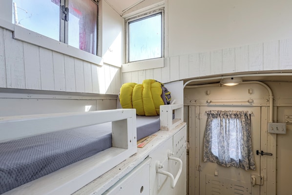A bunk bed with a mattress and pillows, a small window, and a door with a curtain.