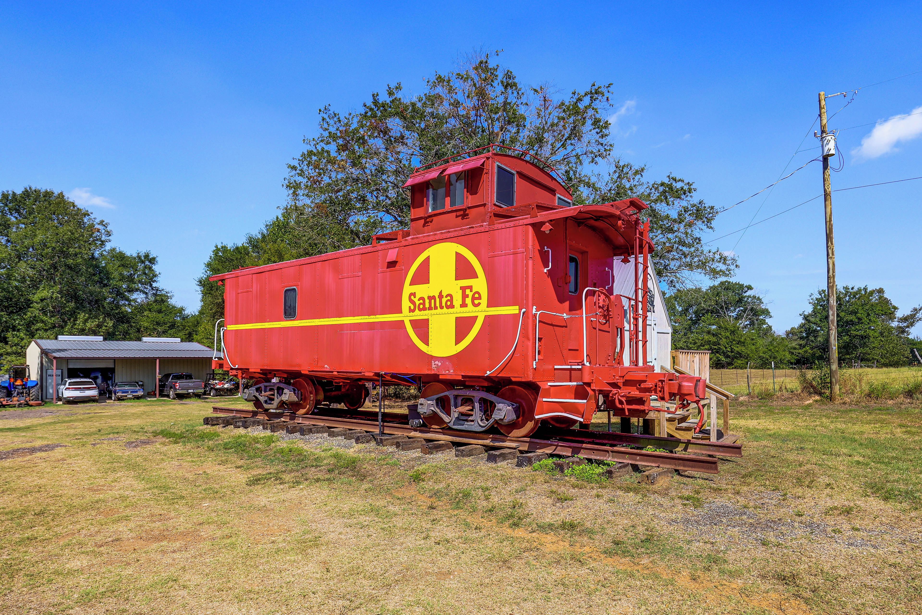 A stationary red train car with 'Santa Fe' branding, situated on tracks with a rural backdrop.