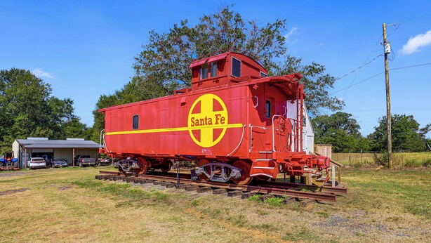 Un vagón de tren rojo estacionado sobre vías, con la marca 'Santa Fe' y un paisaje rural de fondo.