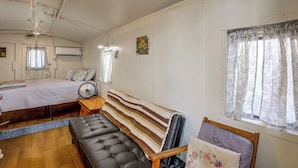 Una habitación con cama, una banca, un ventilador y una ventana con cortinas.