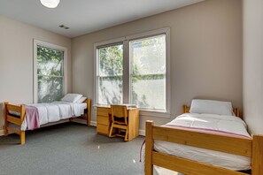 Ein Schlafzimmer mit zwei Einzelbetten, einem Schreibtisch und zwei Fenstern mit Jalousien.