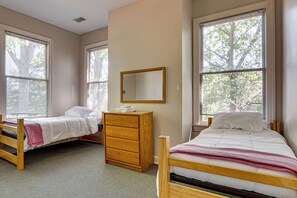 Quarto com duas camas de solteiro, cômoda de madeira e espelho na parede.