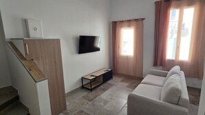 Una sala de estar con un sofá, un televisor de pantalla plana, una pequeña mesa de madera y una escalera.