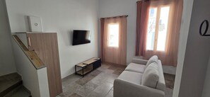 A living room with a sofa, a flat-screen TV, a small wooden table, and a staircase. - Vrbo Property (La Ciotat)