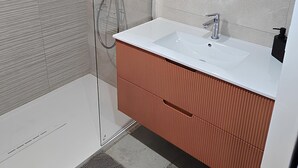 Ein modernes Badezimmer mit Duschkabine aus Glas, einem weißen Waschbecken mit rundem Spiegel und einer Holzkommode.