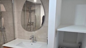 Un baño con lavamanos blanco, espejo y un refrigerador pequeño.