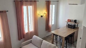 Ein Wohnzimmer mit einer Couch, ein Essbereich mit Tisch und Stühlen sowie eine Küchenzeile mit Arbeitsplatte und Geräten.