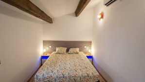 Un dormitorio con cama, vigas de madera, aire acondicionado de pared y una lámpara de noche.