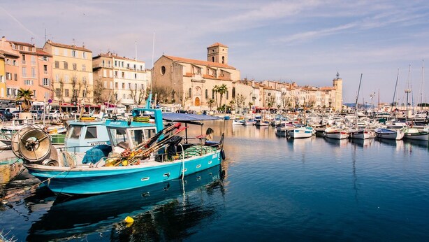Un puerto deportivo con barcos amarrados, un edificio con una torre y un tranquilo paseo marítimo.