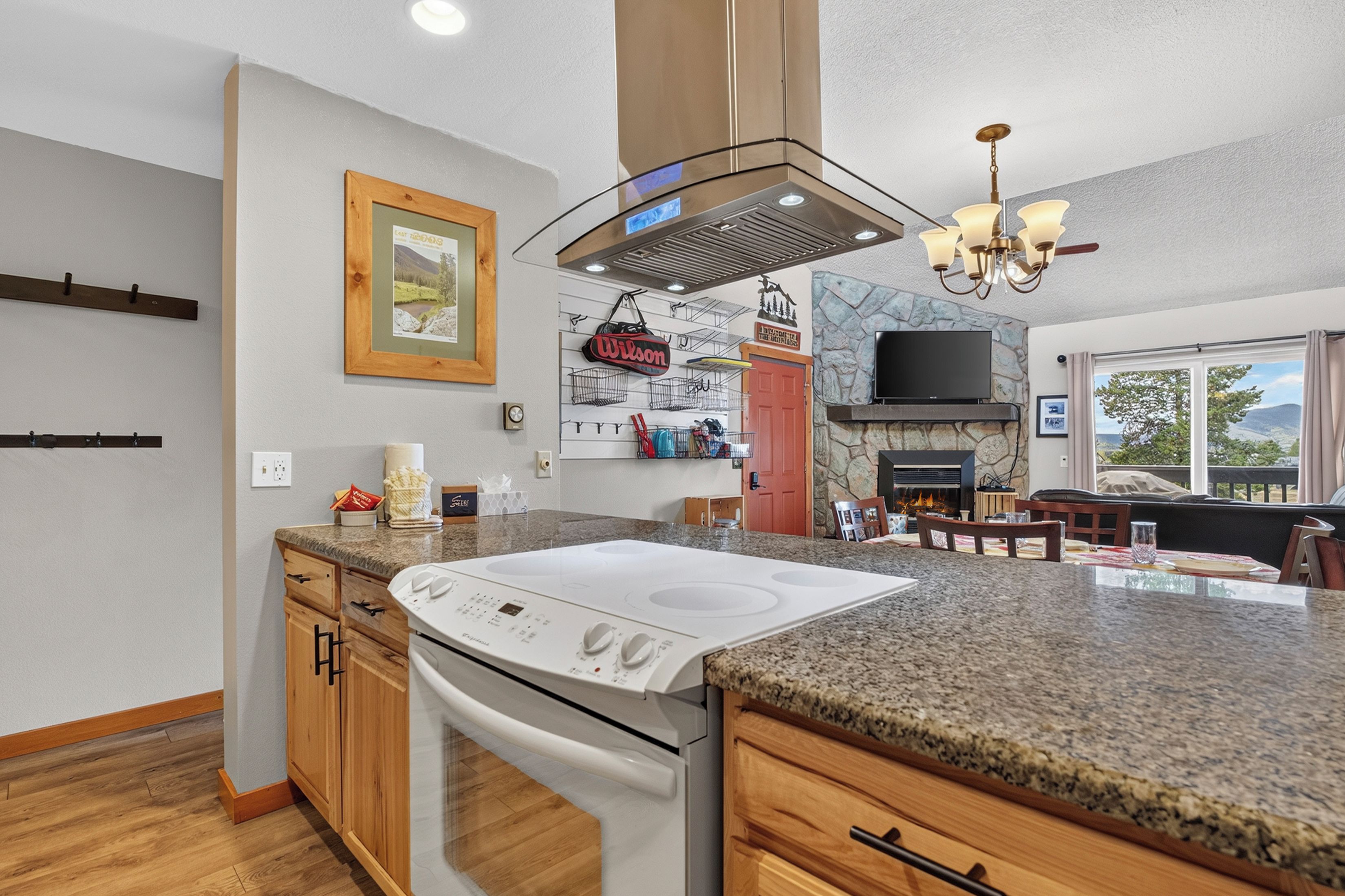A modern kitchen with a built-in stove, granite countertops, wooden cabinets, and a stone accent wall.