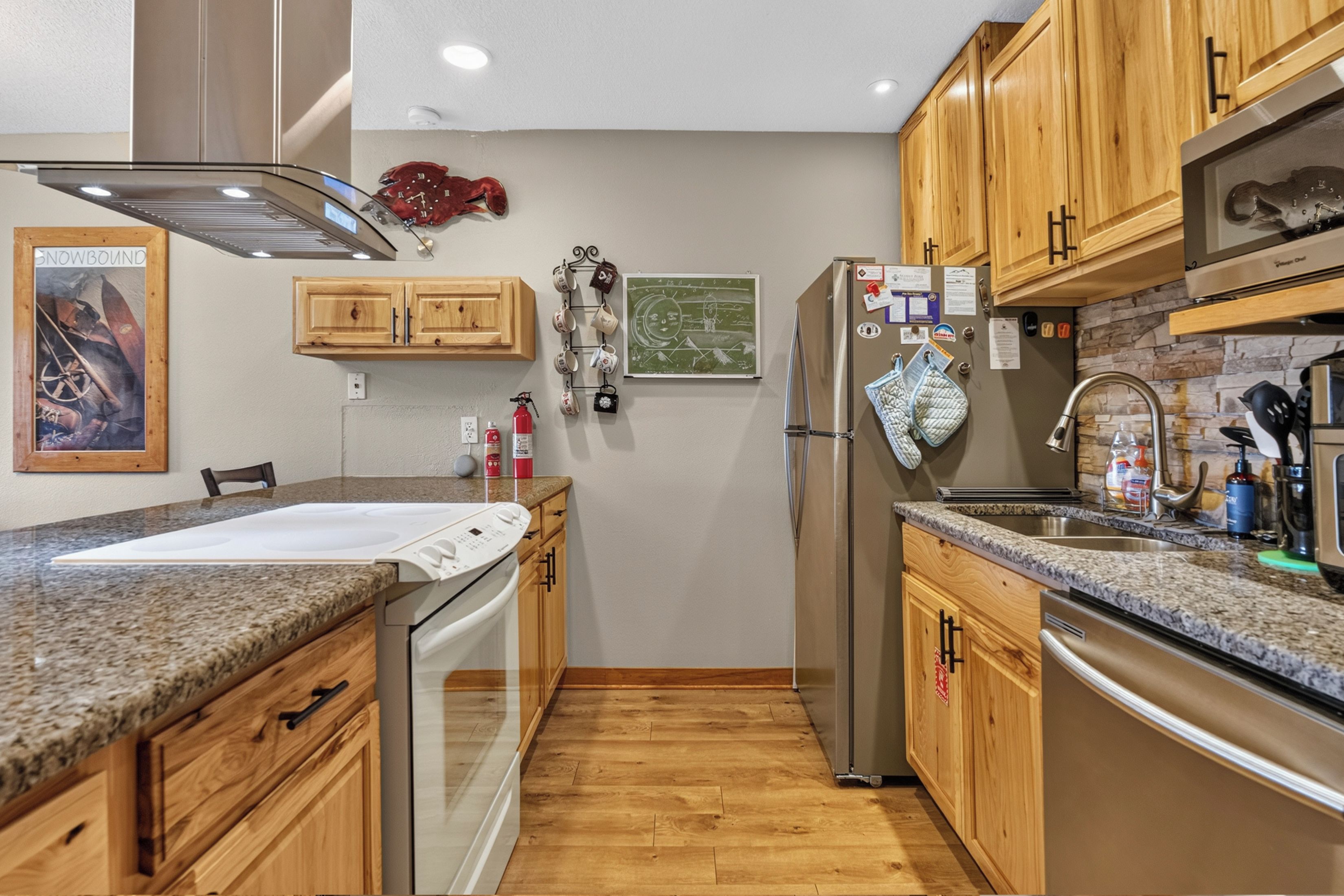Una cocina con armarios de madera, un refrigerador de acero inoxidable, un lavavajillas, encimera de granito y piso de madera.