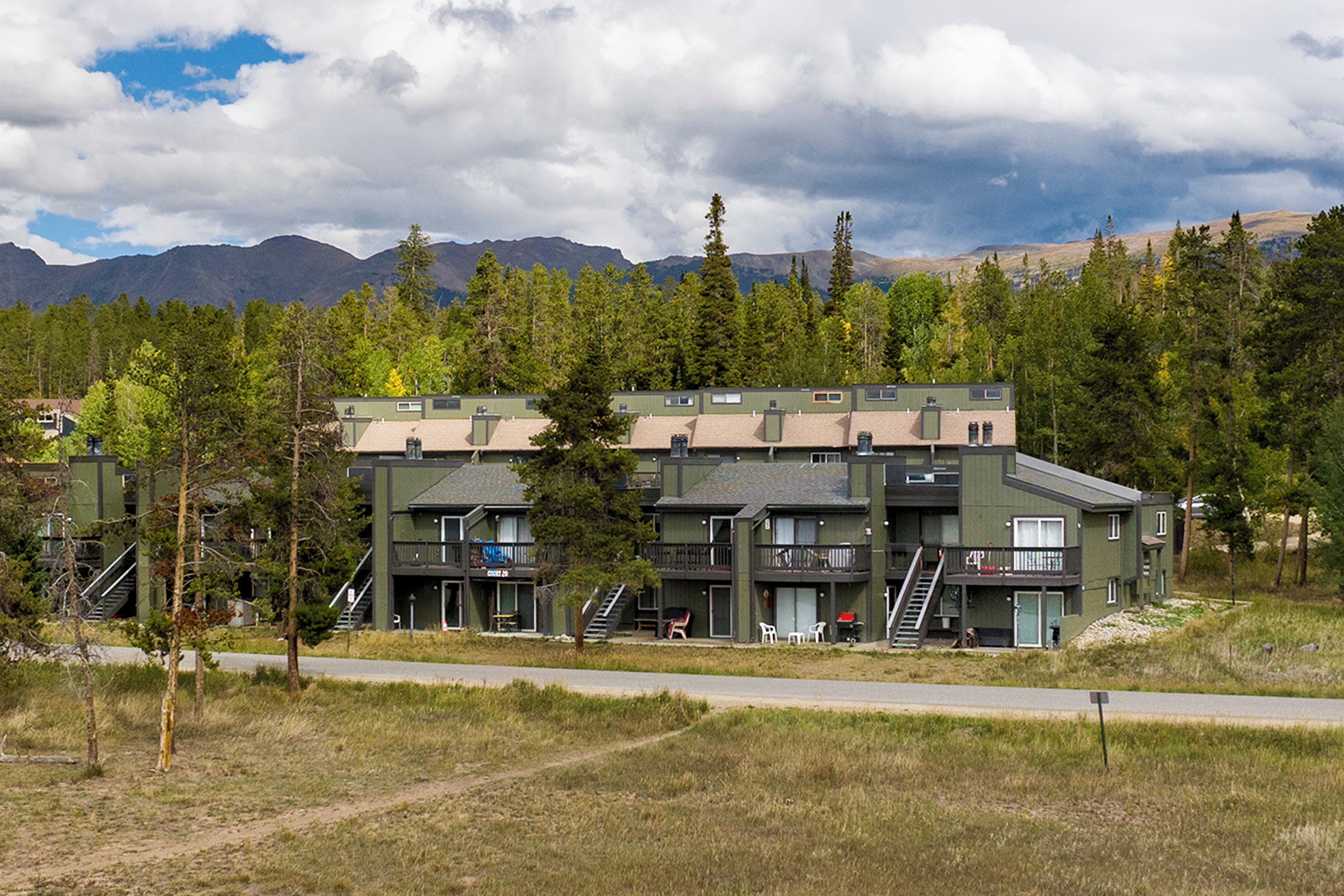 A multi-story building with a green facade, multiple balconies, and a view of mountains in the background.