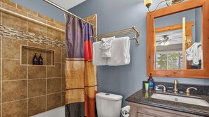 Ein Badezimmer mit Badewanne, Toilette und Waschbecken. Auf dem Waschbecken liegen Pflegeprodukte und über der Toilette ist ein Handtuchhalter angebracht.